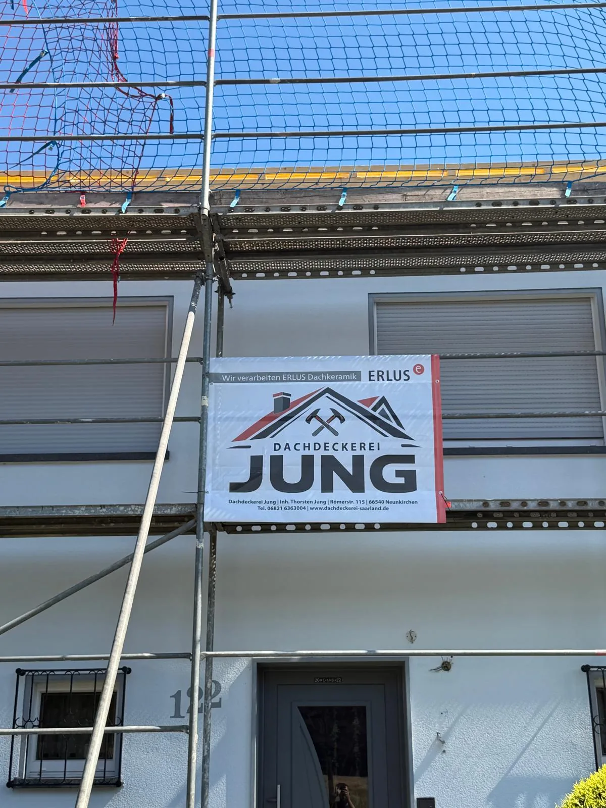 Bauschild der Dachdeckerei Jung mit ERLUS-Logo am Gerüst einer Dachsanierung